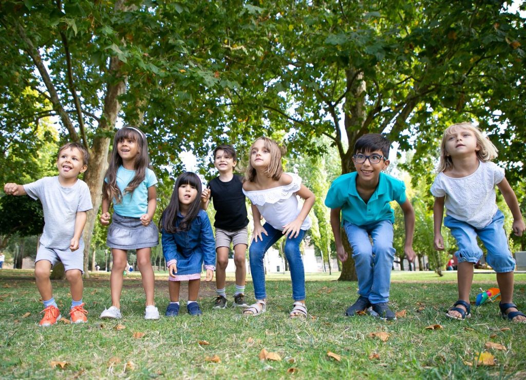 Seven young children getting ready to run in a park